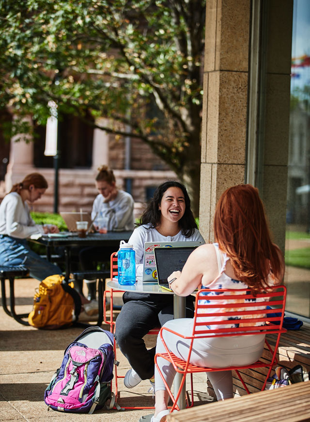 坐在图书馆外的桌子旁，一边学习一边微笑和交谈